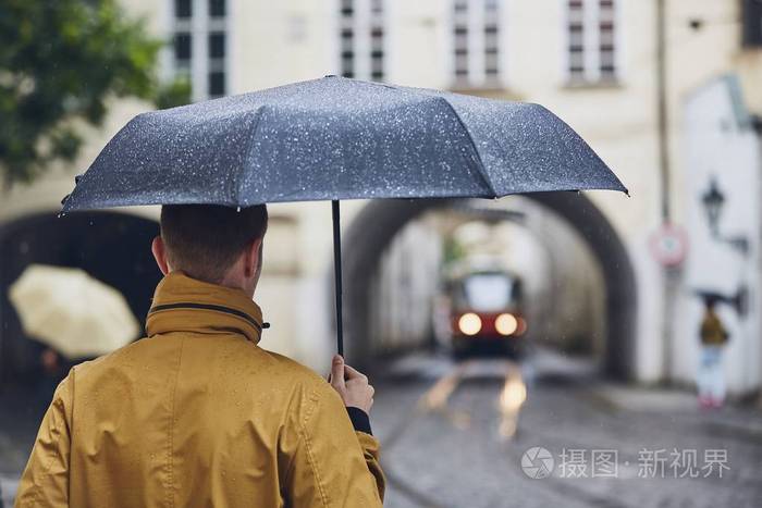 年轻男子抱着雨伞在雨中行走.捷克布拉格古城街