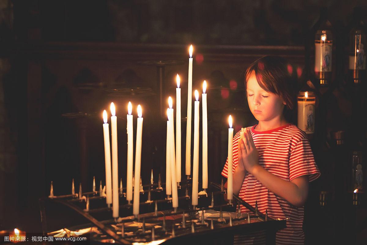 小男孩在东正教教堂祈祷并点燃蜡烛