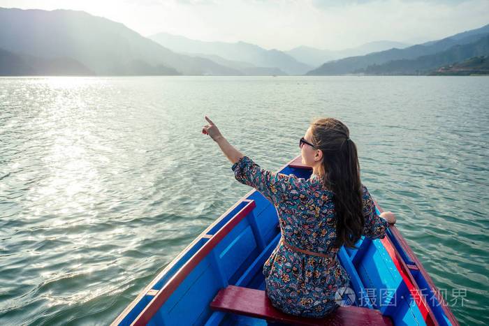 美丽而年轻的女人坐在一条小船上,在山的背景下.