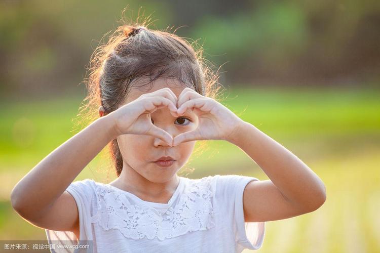 可爱的亚洲小女孩用手在阳光下的田野里制作心形