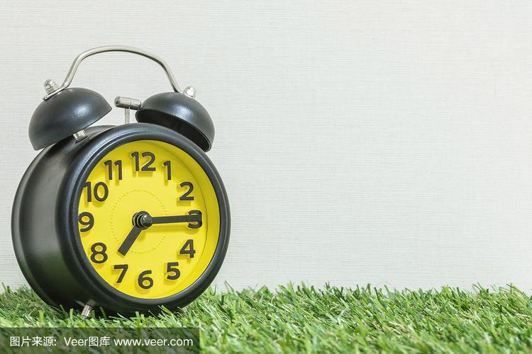 特写黑色和黄色的闹钟装饰显示7点15分或早上7点15分在绿色的人造草