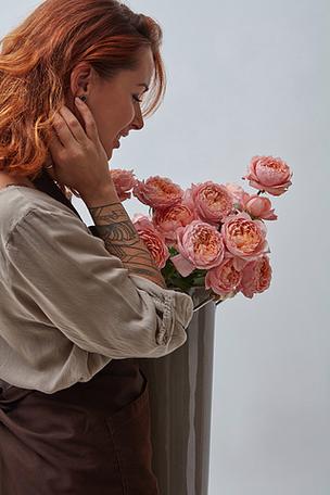有纹身花刺的女孩卖花人在拿着桃红色玫瑰的花束在花瓶的一条棕色围裙