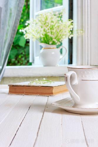 一杯茶或咖啡, 一本书上的白色木制复古表和一束百合花在窗台上, 在