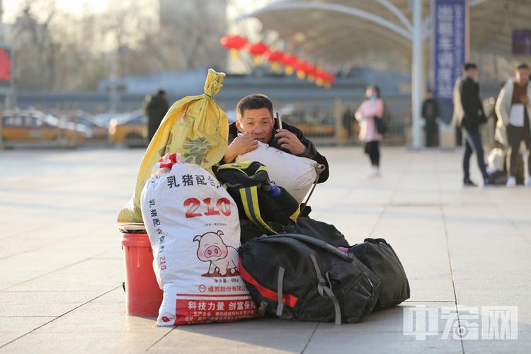 一位旅客坐在大包小包行李旁打电话,在外打工,每年都盼着过年回家.