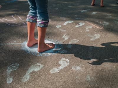 女孩赤脚在人行道上踩粉笔脚印照片