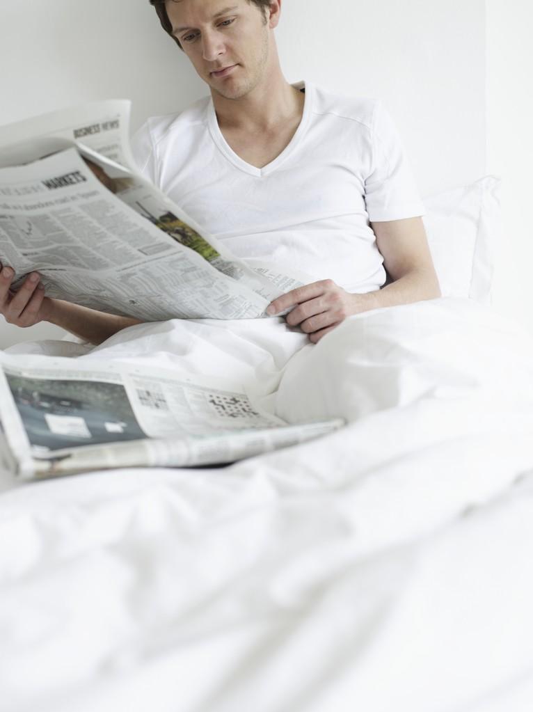 年轻人看报纸,年轻的男人在床上看报纸