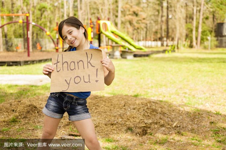 志愿者服务:可爱的小女孩拿着"谢谢"的牌子.当地的公园.