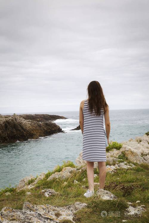 一个年轻的女人在阴天看着一个孤独美丽的岩石海岸