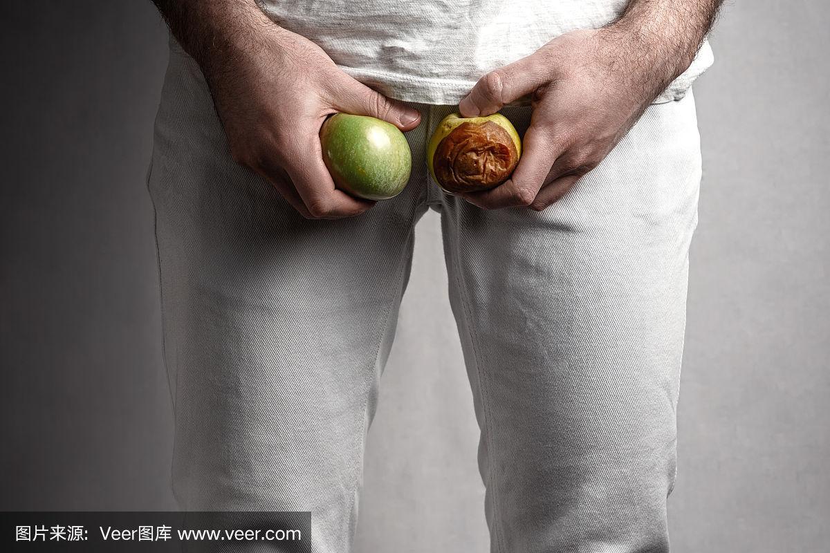 一个男人在生殖器的水平,拿着一个成熟和腐烂的苹果.