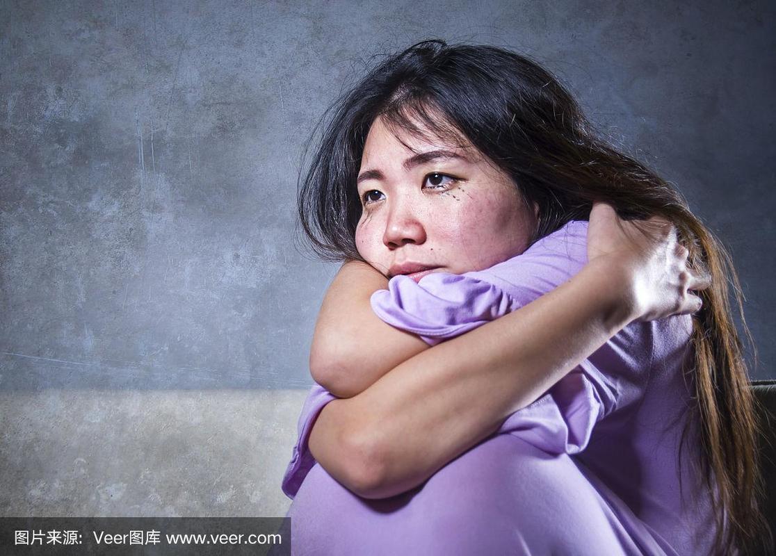年轻的悲伤和沮丧的亚洲华人妇女独自哭泣绝望的坐在家里的沙发,痛苦