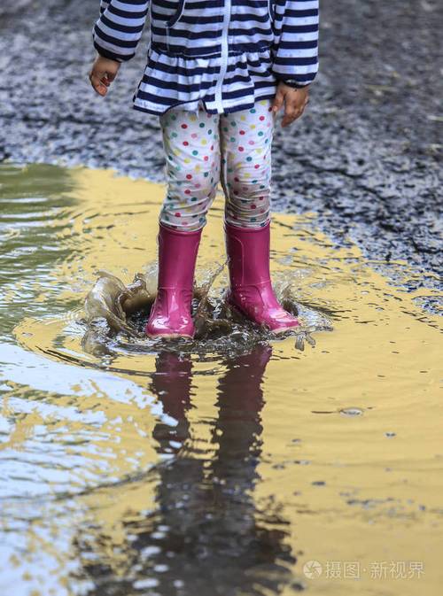 顽皮的孩子在雨后的靴子里跳进水坑