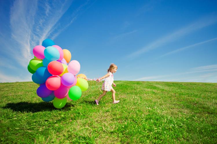 快乐的小女孩抱着五颜六色的气球在一片绿色的草地上玩