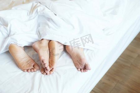 闭上两对恋人的腿脚并排睡觉,在家里的床上拥抱在毯子下的白色床单下