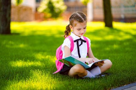 小女生课后背着粉红色的背包坐在草地上看书或学习功课,思考思想,教育
