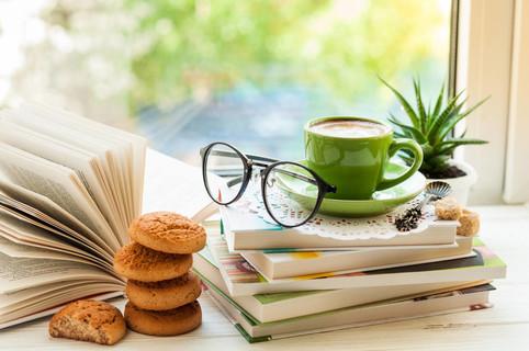 咖啡杯, 翻开的书, 眼镜, 饼干和花与散景的窗口上.阅读和早餐.