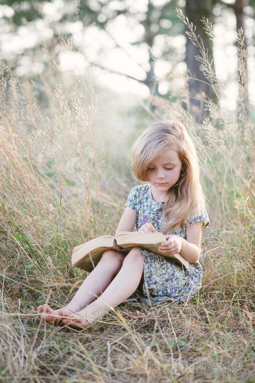 可爱的小女孩坐在草地上和在读书