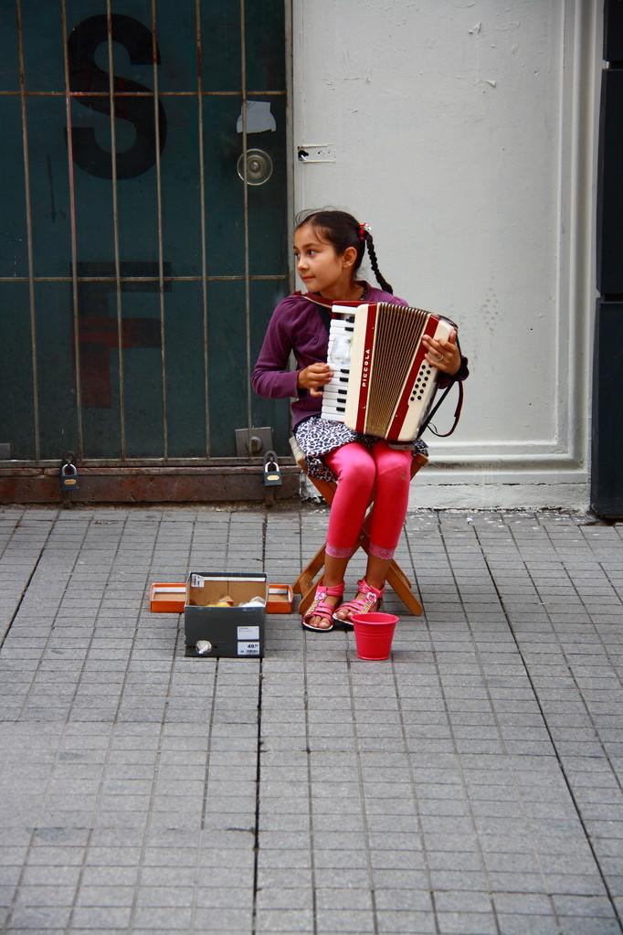 小女孩玩手风琴,手风琴演奏在大街上微笑时的小女孩