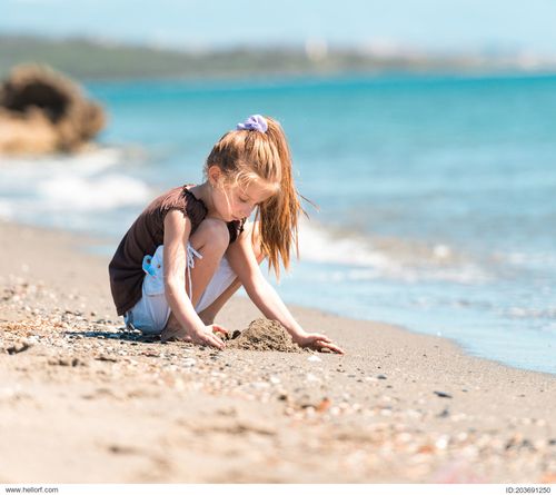 cute little girl sitting on the beach builds a tower of sand