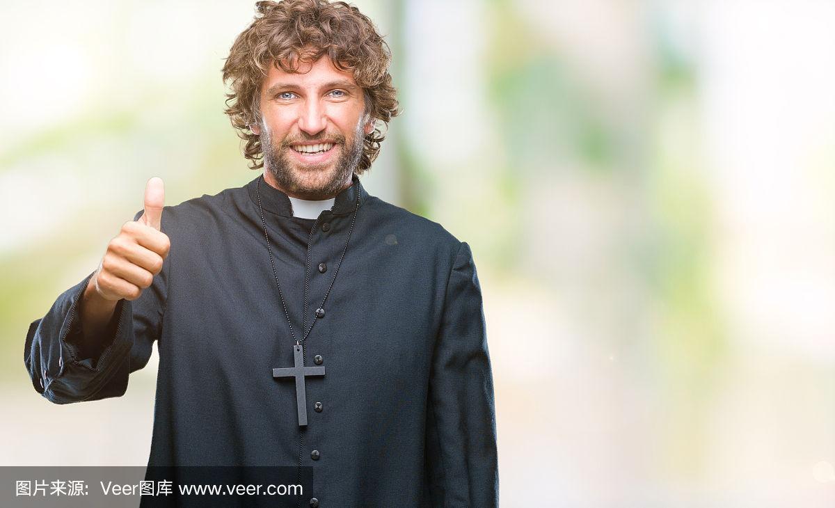 英俊的西班牙天主教神父在孤立的背景做快乐的拇指手势与手.
