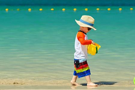 rashguard戴帽子的小孩在沙滩上玩沙滩玩具照片