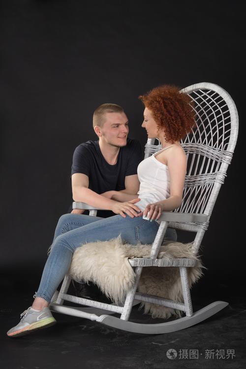 坐在柳条摇椅椅子工作室射击深色背景的年轻夫妇的肖像