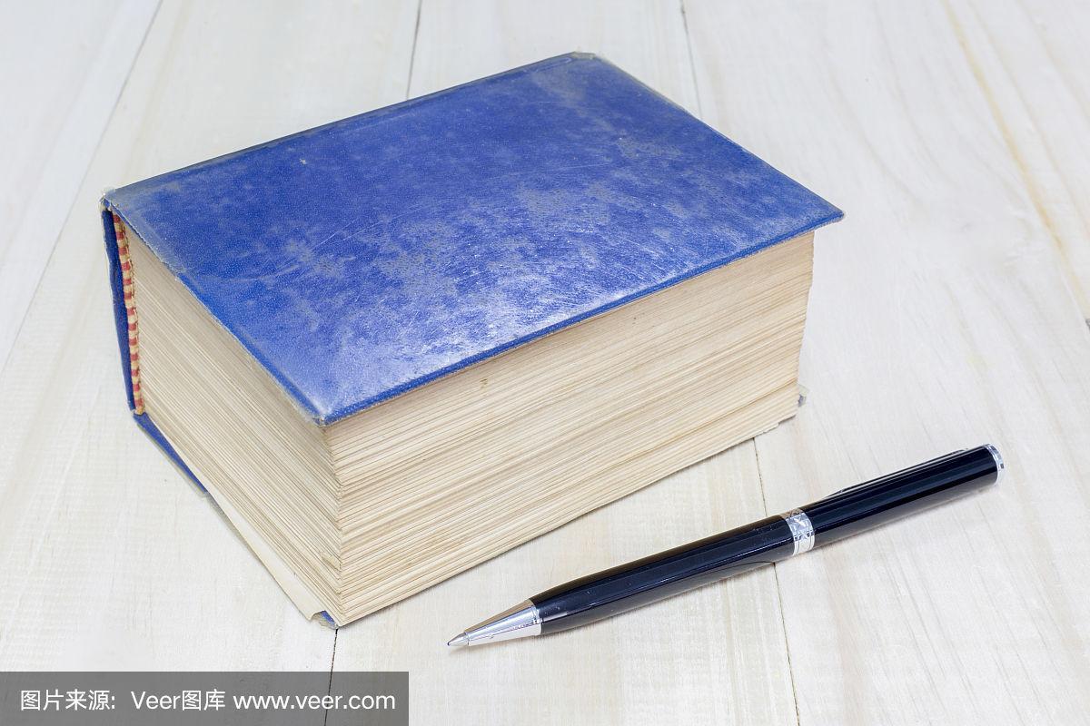 旧厚书蓝色封面和钢笔在木制的背景