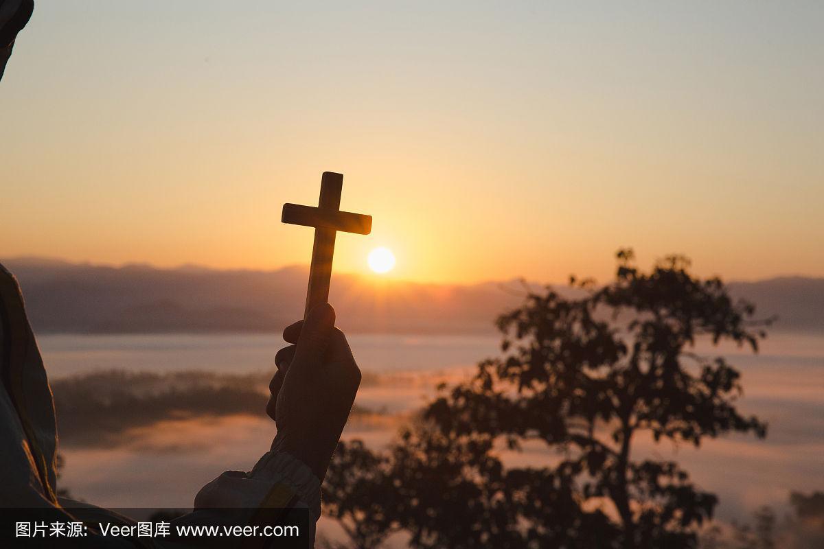 剪影的基督徒男子手中拿着十字架祈祷从上帝的祝福在阳光背景,希望的