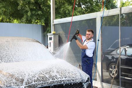 年轻工人在洗车场用高压水射流清洗汽车照片