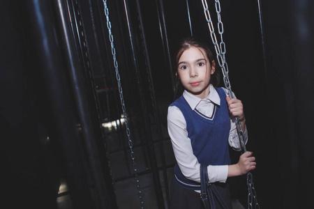 一个穿着校服的小女孩在一个黑暗的房间里,挂着铁链照片