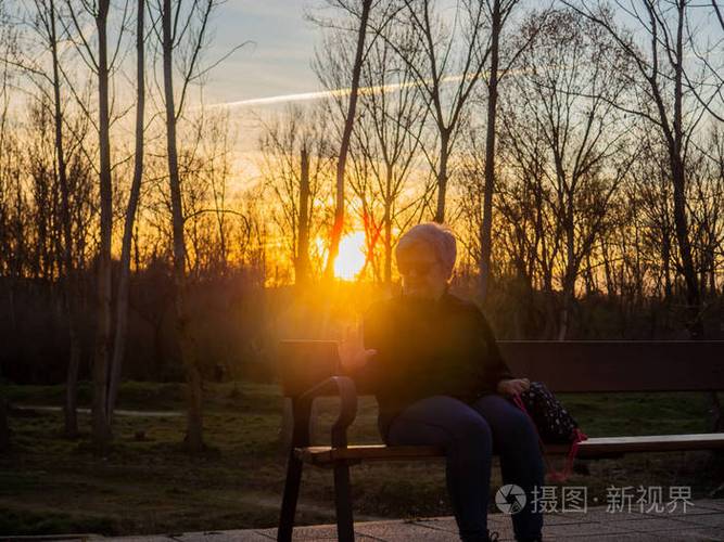 夕阳下一位白发老人坐在公园长椅上看书