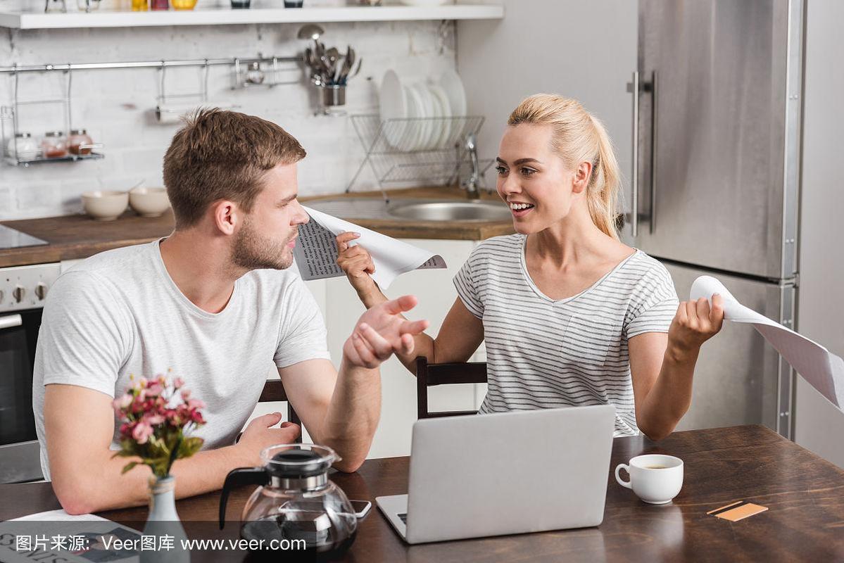 高角度的年轻夫妇交谈和看着对方,同时使用笔记本电脑一起在家里