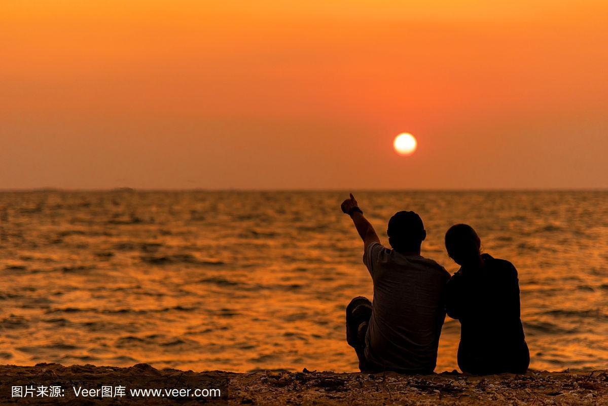 剪影情侣坐在沙滩上,放松相爱和拥抱,日落在海滩上.家庭与生活理念