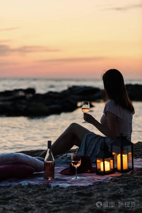 海滩上的浪漫野餐. 一瓶酒杯,蜡烛,格子和枕头. 选择性聚焦.