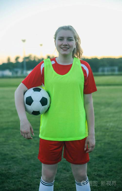 夕阳下一位微笑着拿着足球的女足球运动员的肖像