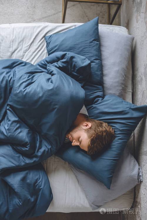 在家里的床上睡在毯子下的年轻英俊男子的最高视图