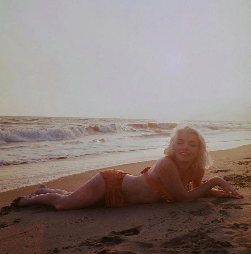 1962年,著名女演员玛丽莲·梦露在海滩上度假,穿着性感的泳装趴在沙滩