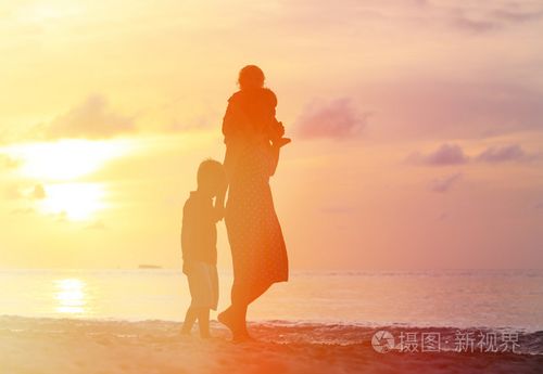 母亲和两个孩子在日落时在海滩上行走