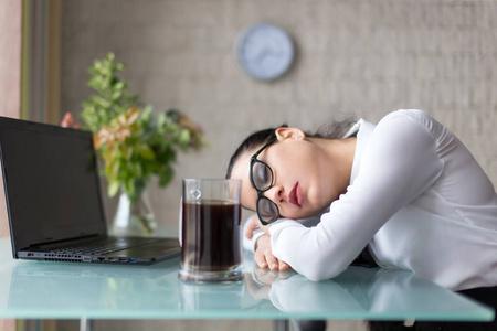 劳累过度的女人睡在办公室的办公桌旁照片