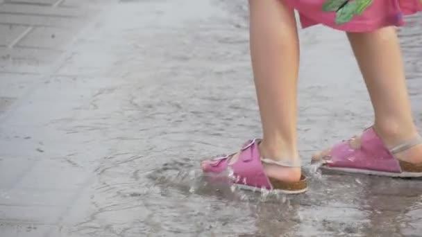 一个女孩穿着粉红色的凉鞋,逐句通过水坑