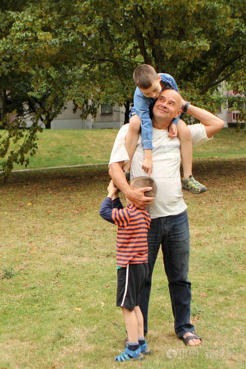 男人爷爷轻轻地抱着孙子第二个男孩坐在他的肩膀上在一个夏日公园里
