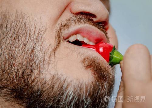 特写显示一个男人咬红辣椒的嘴和牙齿.