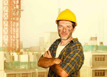 年轻有魅力和自信的承包商或建筑工人,戴着建筑工人安全帽,在建筑工地