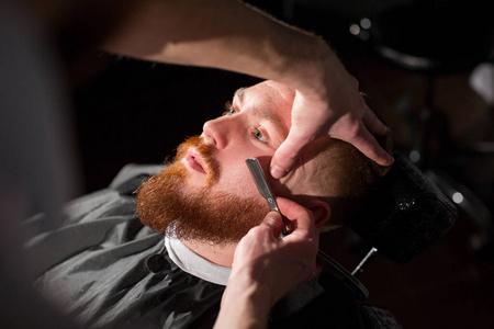 一个英俊的大胡子男人正在理发店被理发师刮胡子.照片