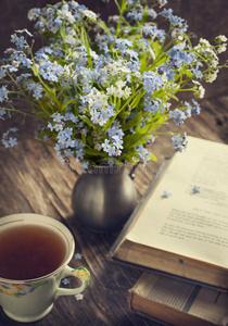 一束夏天的蓝色花朵,一杯茶和一本古书照片