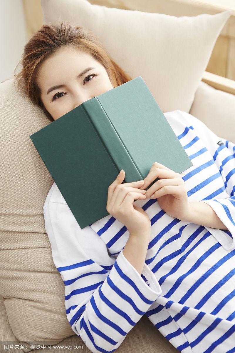 女人躺在沙发上用书盖脸的照片