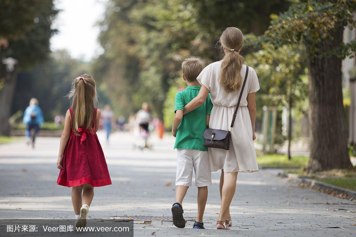 背影年轻的金发长头发的女人走在两个孩子,小女儿和儿子沿着阳光灿烂
