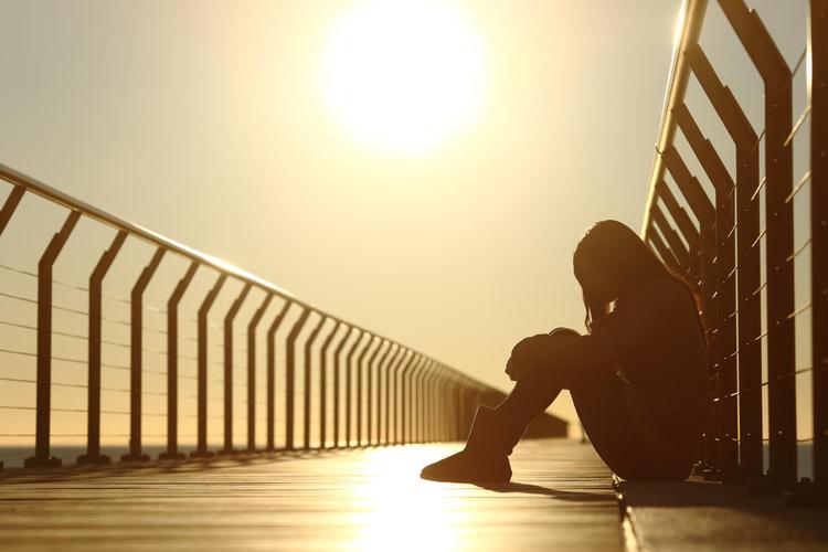悲伤的十几岁的女孩沮丧在日落时分坐在地板上的一座桥在海滩上烦躁