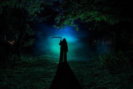 用镰刀在黑暗的雾林中死去.森林里抱着收割者的女人恐怖幽灵照片