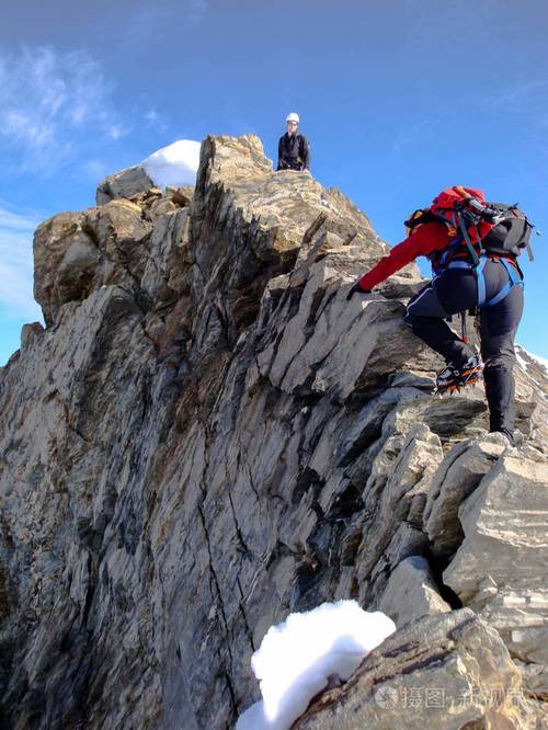 男女登山者沿着一个狭窄的岩石山脊走到一座高峰