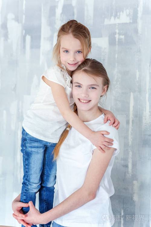 两个快乐的孩子站在灰色纹理的墙壁背景和拥抱可爱的漂亮小女孩拥抱